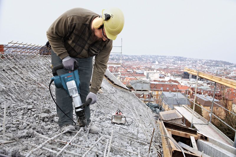 GSH 11 VC Một người mặc thiết bị an toàn đang sử dụng búa phá dỡ để phá vỡ bê tông trên mái nhà.