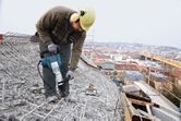 Một người mặc thiết bị an toàn đang sử dụng búa phá dỡ để phá vỡ bê tông trên mái nhà.