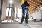 Một người mặc thiết bị an toàn đang sử dụng búa phá dỡ để phá sàn bê tông.