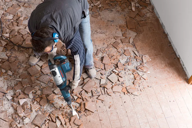 GSH 9 VC Một người mặc đồ bảo hộ đang dùng búa phá dỡ để phá gạch lát sàn.