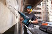 Một người mặc thiết bị an toàn đang sử dụng búa phá dỡ để phá bê tông tại công trường xây dựng.