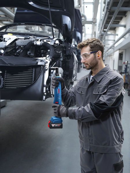 Một người mặc đồ bảo hộ đang siết chặt bu lông trên khung xe bằng dụng cụ điện không dây.