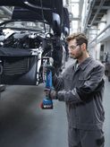 Một người mặc đồ bảo hộ đang siết chặt bu lông trên khung xe bằng dụng cụ điện không dây.
