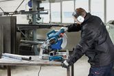 Một người mặc đồ bảo hộ đang cắt ống kim loại bằng cưa cắt kim loại.