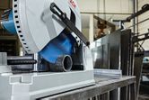 Máy cắt kim loại đang cắt qua một ống kim loại tròn trong một xưởng công nghiệp.