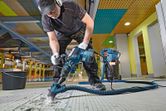 Một người mặc đồ bảo hộ đang sử dụng búa phá dỡ để phá vỡ sàn gạch.