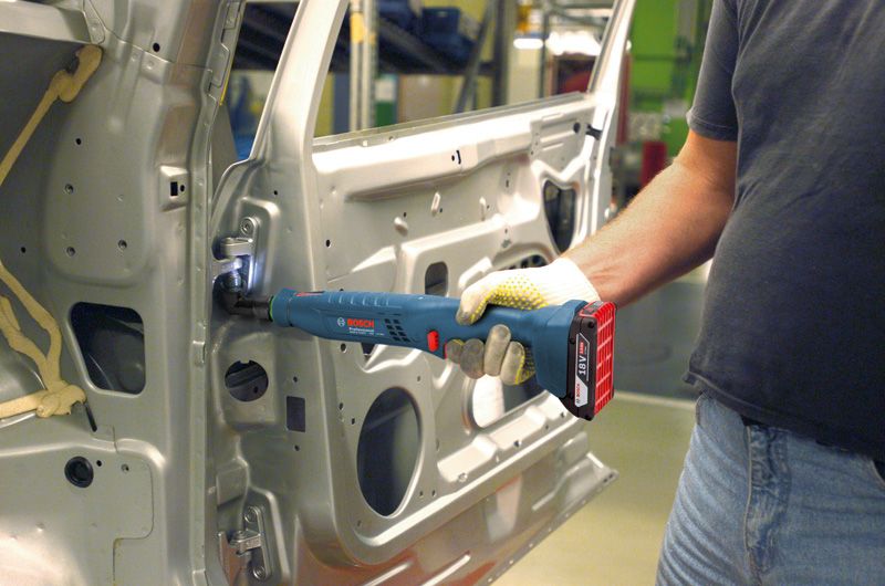 Người đeo thiết bị an toàn sử dụng một công cụ không dây để siết chặt bản lề bên trong cửa ô tô.