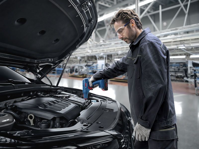 Một người mặc đồ bảo hộ đang sử dụng súng nhiệt trên dây chuyền lắp ráp ô tô.