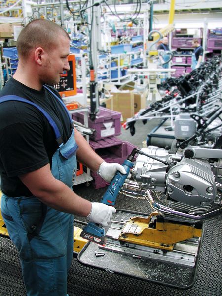 Một người mặc đồ bảo hộ đang sử dụng dụng cụ điện để lắp ráp động cơ xe máy.