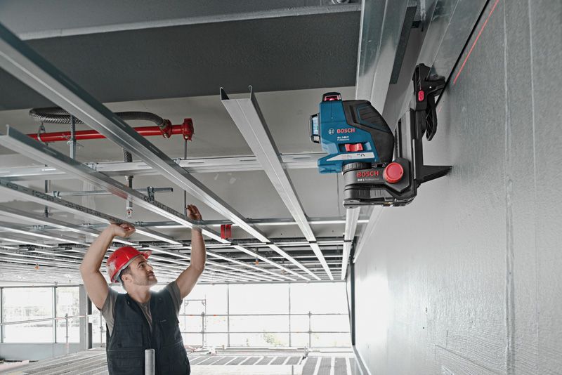 BM 1 Một người đeo thiết bị an toàn đang căn chỉnh khung trần nhà bằng dụng cụ cân bằng laser trên giá đỡ đa năng.