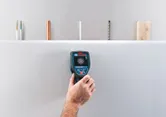 Một người sử dụng máy dò tường để kiểm tra phía sau bề mặt tường thạch cao.