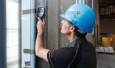 Một người mặc thiết bị an toàn đang quét bức tường bê tông bằng máy dò tường.