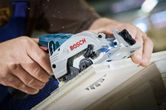 Một người đang cắt một tấm ván gỗ bằng máy cưa tròn không dây.