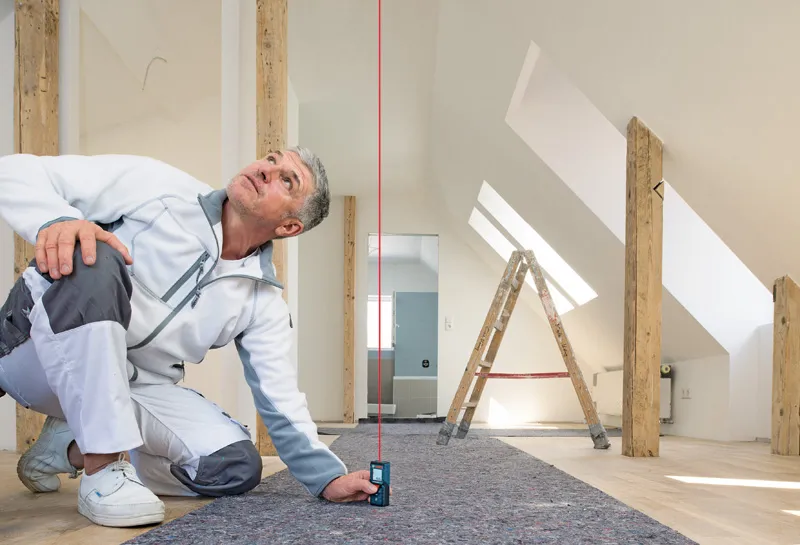 Một người sử dụng thước đo laser để kiểm tra độ thẳng đứng trong một căn phòng gác mái sáng sủa.