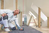Người mặc quần áo lao động sử dụng máy đo laser để kiểm tra khoảng cách theo chiều thẳng đứng trong một căn phòng đã được cải tạo.