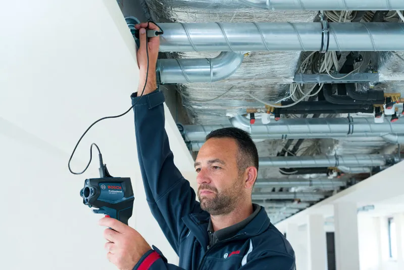 Một người đang kiểm tra đường ống thông gió trên trần nhà bằng camera kiểm tra.