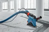 Máy đục tường có ống hút bụi đang cắt rãnh trên sàn bê tông.