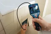 Một người đang sử dụng camera kiểm tra để xem xét các đường ống phía sau gạch ốp tường phòng tắm.