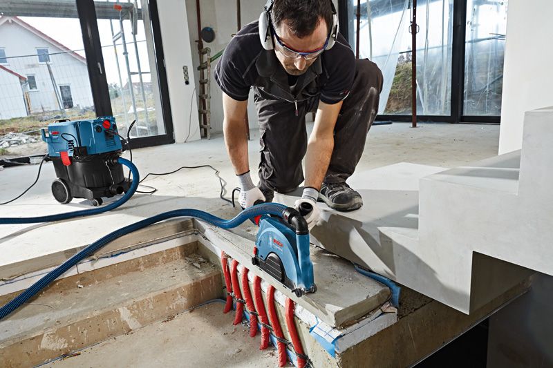 Một người mặc thiết bị an toàn sử dụng máy đục tường trên bê tông phía trên các đường ống lộ thiên.