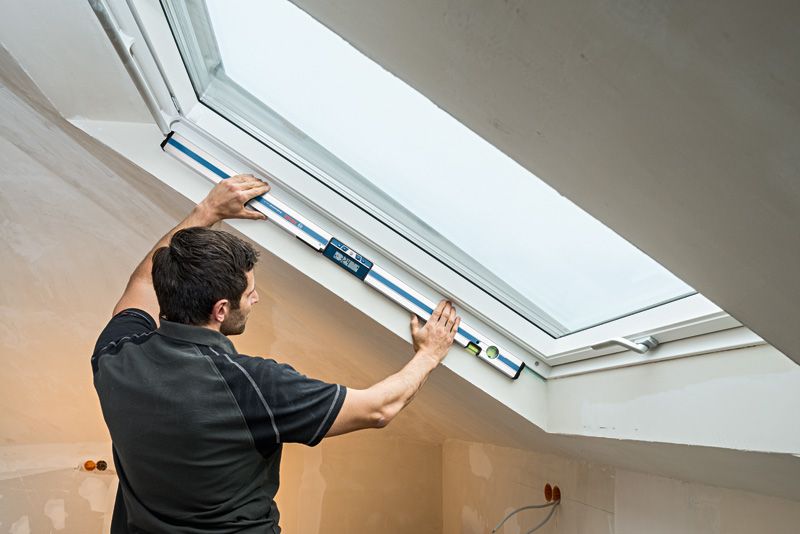 Người đang đo góc cửa sổ bằng máy đo độ nghiêng kỹ thuật số trong một căn phòng gác mái đã hoàn thiện.