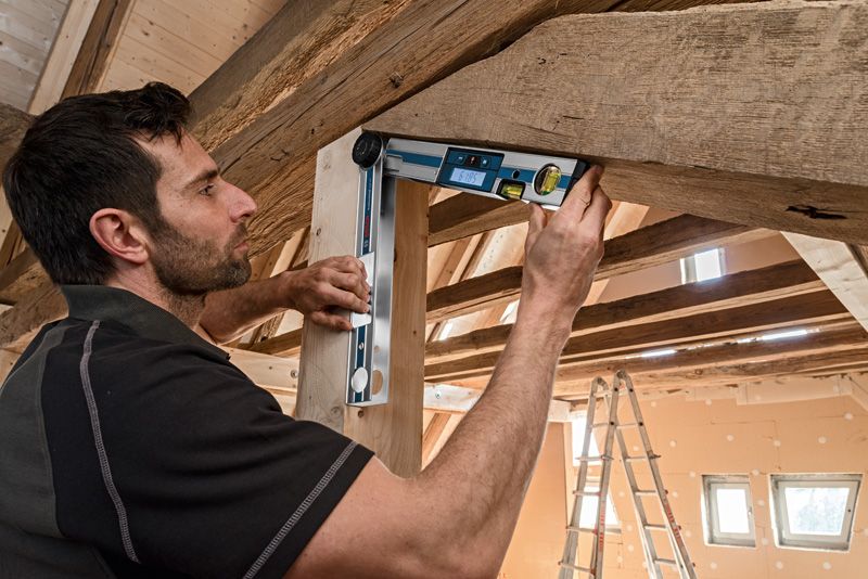 Một người kiểm tra góc của một thanh gỗ bằng máy đo độ nghiêng kỹ thuật số dưới mái gỗ.