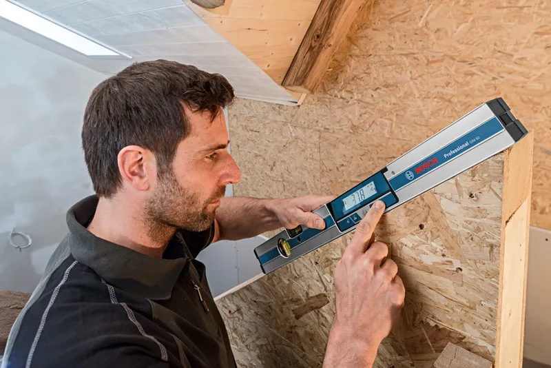 Một người sử dụng máy đo độ nghiêng kỹ thuật số để đo góc của một cấu trúc bằng gỗ.