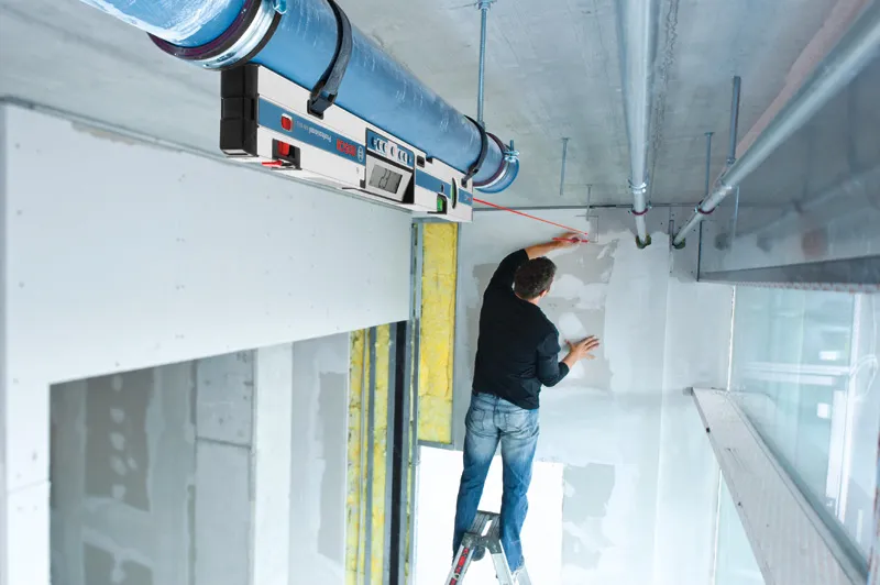 Một người đứng trên thang đánh dấu bức tường bằng máy đo độ nghiêng kỹ thuật số để căn chỉnh.