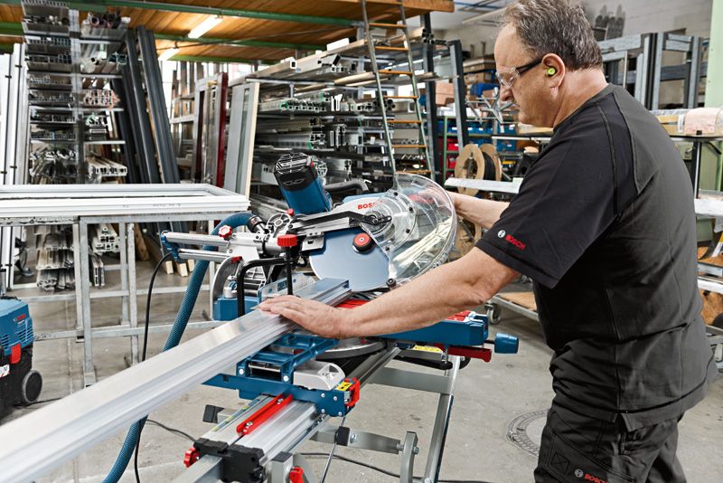 Một người mặc đồ bảo hộ đang vận hành máy cưa góc trượt để cắt một hình dạng kim loại.