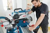 Một người mặc đồ bảo hộ đang vận hành máy cưa góc trượt để cắt gỗ.