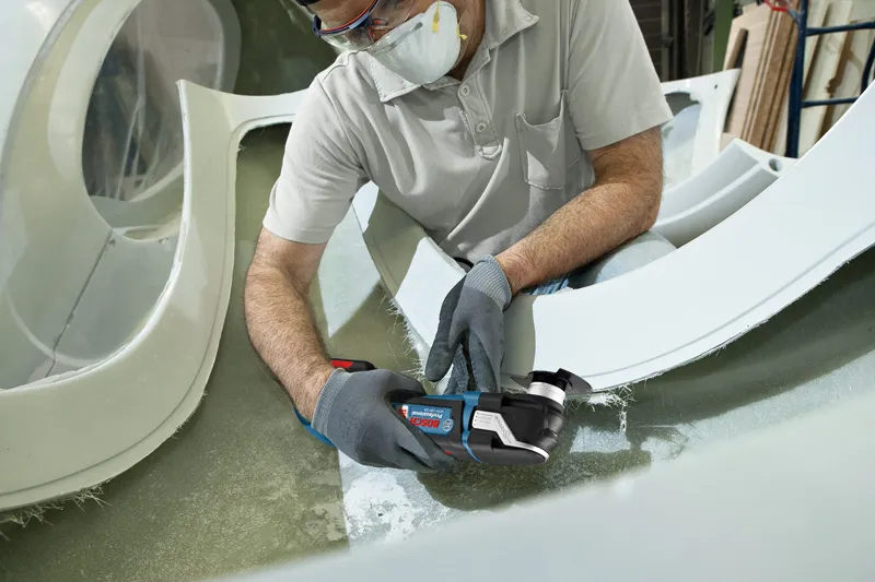 Một người mặc đồ bảo hộ đang cắt sợi thủy tinh bằng dụng cụ đa năng không dây.