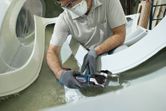 Một người mặc đồ bảo hộ đang cắt sợi thủy tinh bằng dụng cụ đa năng không dây.