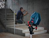 Người quỳ bên cạnh cầu thang sử dụng một công cụ cân bằng laser chiếu một đường màu đỏ lên bức tường bê tông.