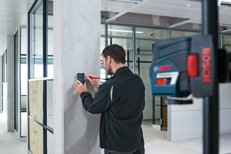 LR 6 Một người đang căn chỉnh máy thu tia laser trên một cột bê tông trong một văn phòng hiện đại.