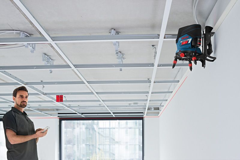 RM 3 Một người vận hành thiết bị cân bằng laser gắn trên tường để căn chỉnh khung trần nhà.