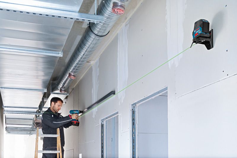 Người sử dụng máy khoan để lắp thanh ray kim loại, được hướng dẫn bằng công cụ cân bằng laser màu xanh lá cây.