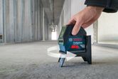 Một người đang điều chỉnh máy cân bằng laser trên sàn bê tông ở hành lang chưa hoàn thiện.