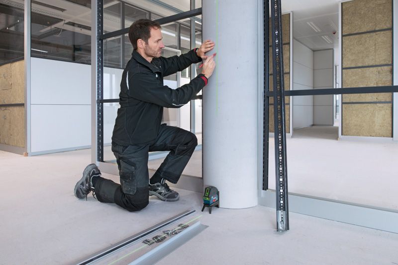 Một người mặc đồ bảo hộ đang đánh dấu một cột bê tông bằng máy cân bằng laser.