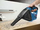 Một người sử dụng máy hút bụi không dây để hút mảnh vụn trên bàn làm việc.