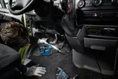 Một người mặc đồ bảo hộ đang vệ sinh sàn xe bằng máy hút bụi không dây.