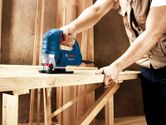 Một người sử dụng máy cưa lọng để cắt một tấm ván gỗ tại công trường xây dựng.