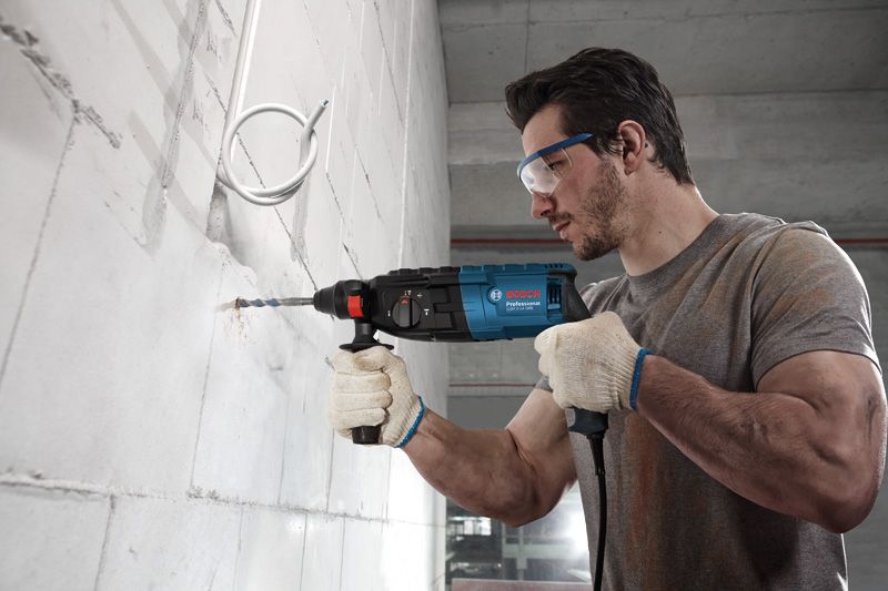 GBH 2-24 DRE Một người mặc đồ bảo hộ đang khoan vào tường bê tông bằng một dụng cụ điện.