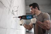 Một người mặc đồ bảo hộ đang khoan vào tường bê tông bằng một dụng cụ điện.