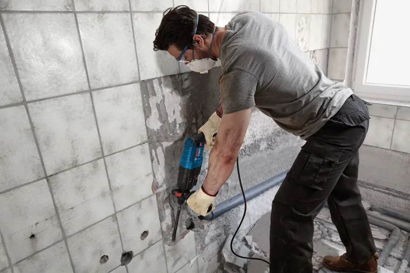 GBH 2-24 DRE Một người mặc đồ bảo hộ đang sử dụng dụng cụ điện để tháo gạch ốp tường.
