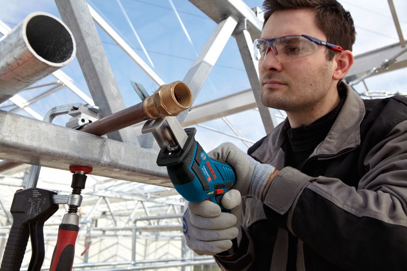 Một người mặc thiết bị an toàn đang sử dụng máy cưa lọng không dây để cắt một ống kim loại.