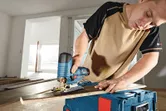Một người đang cắt một tấm ván gỗ bằng máy cưa lọng không dây trên hộp dụng cụ.