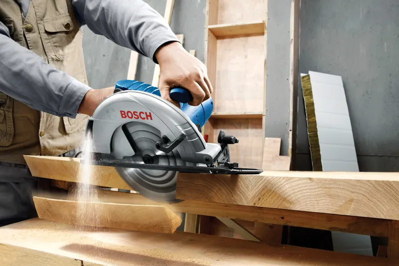 GKS 235 Turbo Một người đang điều khiển máy cưa tròn cắt qua những tấm gỗ dày trong một xưởng.