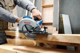 Một người đang điều khiển máy cưa tròn cắt qua những tấm gỗ dày trong một xưởng.