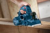 Một người sử dụng máy bào màu xanh để làm phẳng bề mặt của một thanh gỗ.