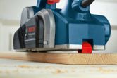 Máy bào điện đang làm phẳng tấm ván gỗ trên bàn làm việc.