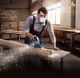 Một người mặc đồ bảo hộ đang bào một thanh gỗ trong xưởng.